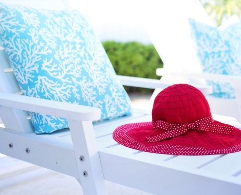 White Lounge Chair with Blue and white pillow and red sunhat, outdoors